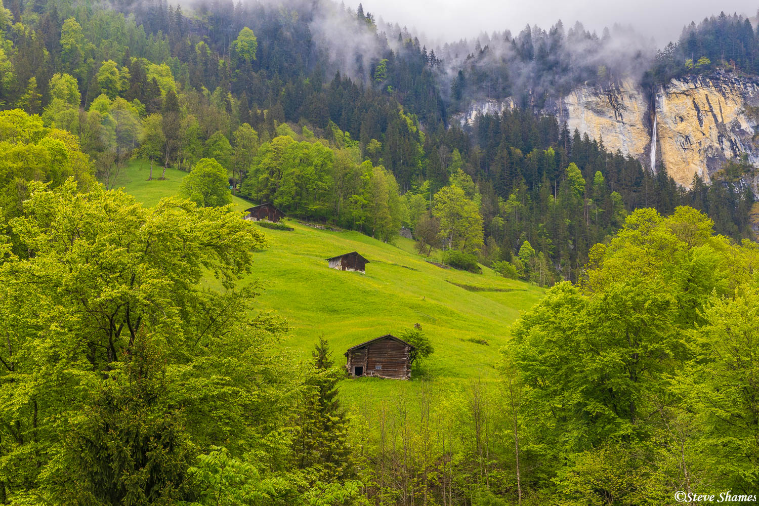 Little Swiss farm buildings, with a waterfall in the background.
